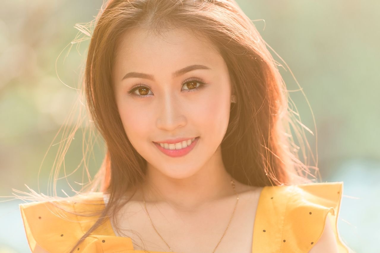 Portrait of a cheerful young woman smiling warmly outdoors with natural sunlight.